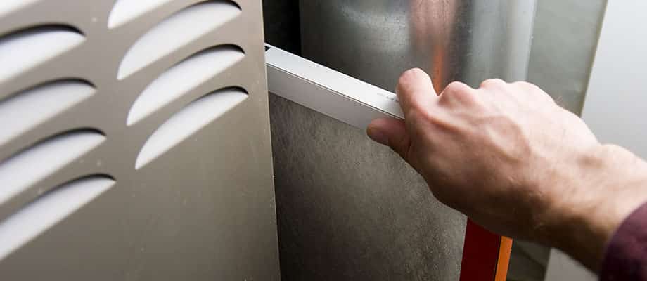 A man removes a dirty air filter from an HVAC system